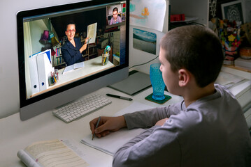 Young boy watching online class, live streaming, sitting at his desk, taking notes. Concept...