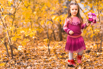 Cute little girl in autumn park with pink flower bouquet