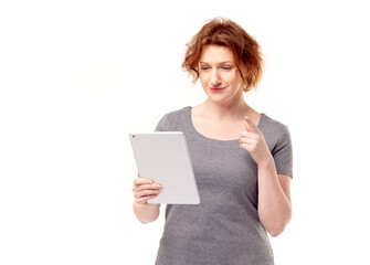 Red haired adult mature woman in gray dress looking at mobile tablet in her hands 