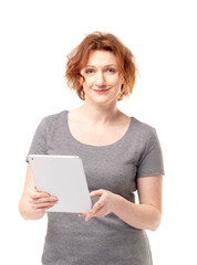 Red haired adult mature woman in gray dress with mobile tablet in her hands smiling