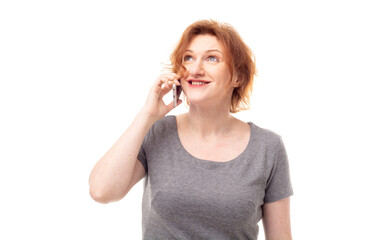 Red haired adult mature woman in gray dress talking on the phone with happy expression, delighted