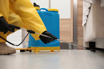 Pest control worker spraying pesticide under furniture indoors, closeup