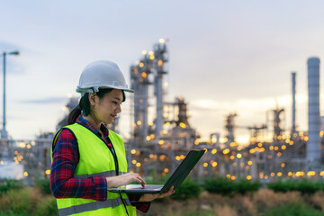 Asian woman petrochemical engineer working at night with notebook Inside oil and gas refinery plant...