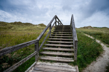 Fototapeta na wymiar wooden jetty for direction beach through the dunes on a cloudy sky