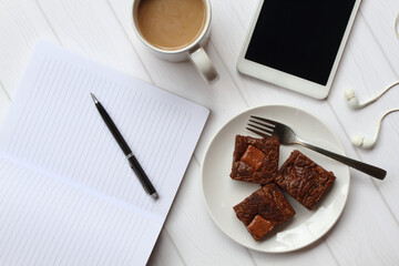 Blank screen tablet with earphone, book and pen, a glass of latte, and a plate of brownies on white background