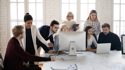 Focused diverse businesspeople gather at shared workplace brainstorm work together on computer discussing business project. Colleagues coworkers collaborate in coworking office. Teamwork concept.