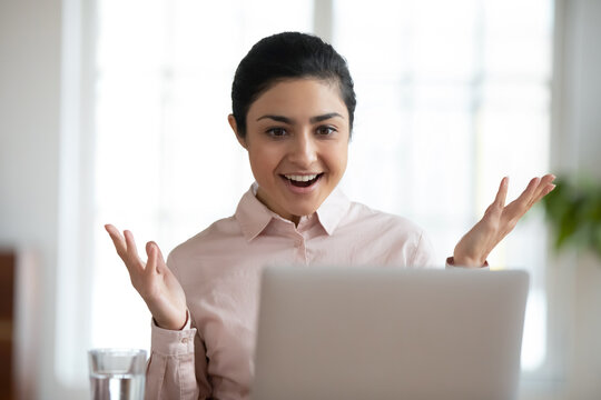 Happy excited young indian woman look at laptop screen surprised by good news on gadget online. Smiling overjoyed millennial ethnic female amazed by unexpected promotion or sale offer on computer.