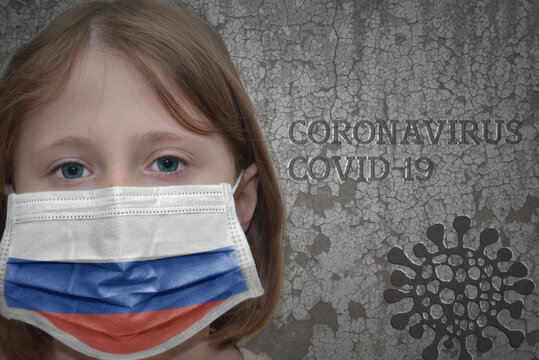 Little girl in medical mask with flag of russia stands near the old vintage wall with text coronavirus, covid, and virus picture. Stop virus concept