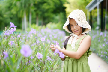 Asian child cute or kid girl smile wearing hat catch and prop up beautiful blooming purple flower in nature tree meadow or green plant garden and public park on spring field flowers and summer season