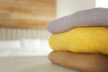 Stack of knitted sweaters on white table indoors, closeup. Space for text