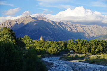 sun setting on the church bell and mountains of the Southern Alps, France by the river