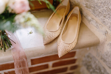 Bride's ballet flats with shiny stones on the windowsill by the stone wall.
