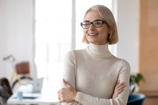 Smiling millennial Caucasian woman worker look in distance thinking dreaming of career success or promotion. Happy young businesswoman in glasses visualize new opportunities. Business vision concept.