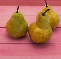 Three large ripe pears on a pink wooden tray. There are specks on the yellow peel. Close-up. Side view.
