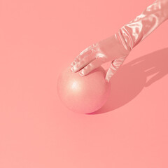 Minimal fashion still life scene. Gloved hand holds a ball. Stylish isometric space, Pink aesthetic. Holidays, christmas, winter, parties concept