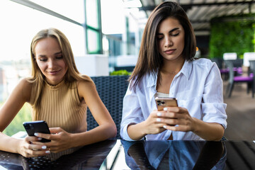 Two friends women enjoying coffee together in a coffee shop and using phone