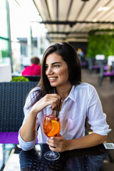 Young pretty smiling woman holding the glass of Aperol Spritz cocktail in cafe