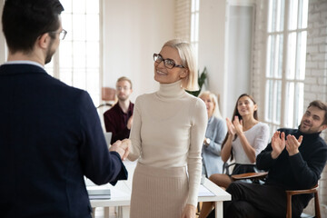 Diverse smiling business partners shake hands at meeting closing deal after successful negotiations. Male boss CEO handshake happy female colleague greeting congratulating with promotion or success.