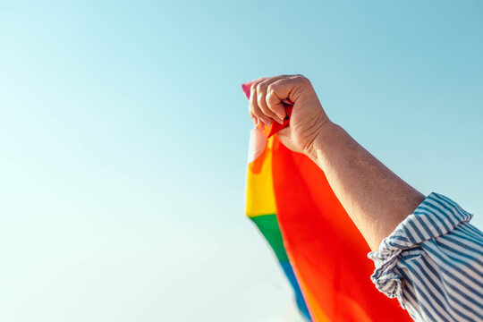 Colorful rainbow gay pride flag being waved in the breeze by a hand. Freedom and love concept.