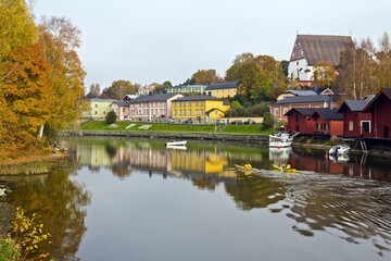 Obraz premium PORVOO, FINLAND - OCTOBER 15, 2015. Two men in canoe sailing in the river reflecting houses on the embankment and yellow trees in autumn in Porvoo, Finland.