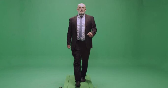 Studio, slow motion, green screen, a suited mature man marches on the treadmill, London, UK