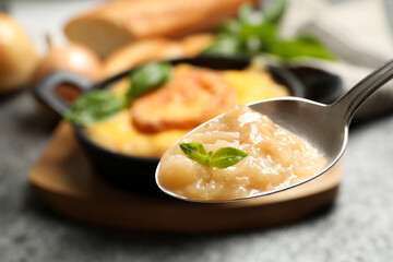 Spoon with fresh homemade french onion soup over bowl, closeup. Space for text