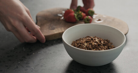 man hand place white bowl with chocolate granola, strawberries and glass for yogurt on a concrete countertop