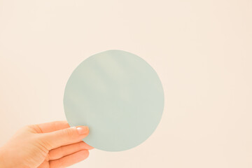 Round blue card with copy space in the hand of a young woman. Pastel blue color postcard layout. Informational round plate about a discount, opening, new product, advantageous offer.