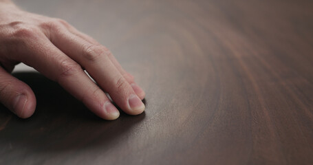 man hand checking toned walnut table surface with oil finish