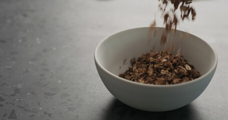 chocolate granola fall into white bowl on terrazzo surface