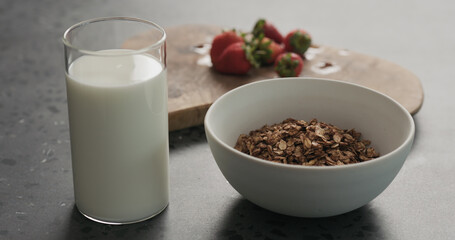 white bowl with chocolate granola, strawberries and glass of yogurt on a concrete countertop