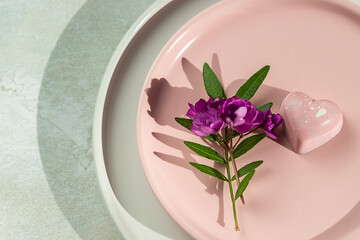 Heart shaped pink chocolate truffle and flowers on a pink plate on a light gray concrete background. Valentine Day, love, dating concept.
