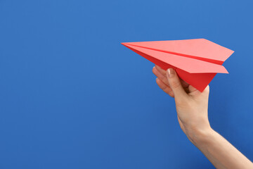 Woman holding paper plane on blue background, closeup. Space for text