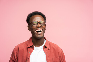 Laughing positive young Afro American man in red shirt in good mood, poses at camera with closed...