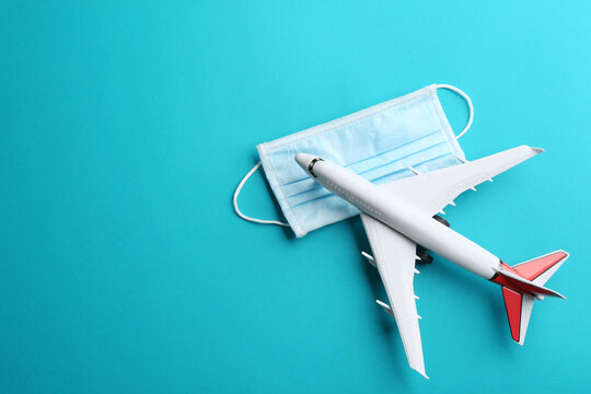Toy airplane and protective mask on light blue background, flat lay with space for text. Travelling during coronavirus pandemic