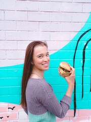 Smiling girl with burger on bright wall background for advertising