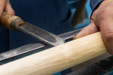hands hold a chisel for processing on the turning machine of a wooden bar