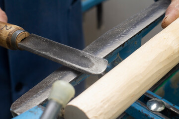 hands hold a chisel for processing on the turning machine of a wooden bar