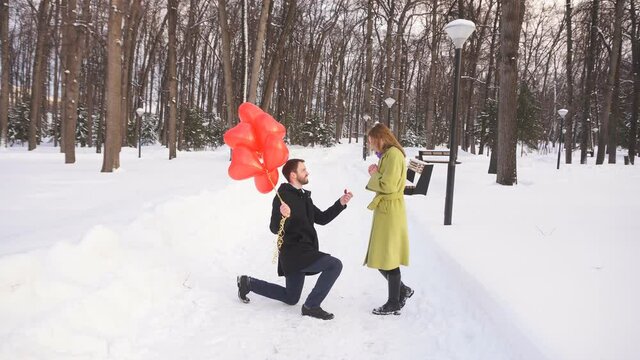 young man gets down on one knee and proposes to his beautiful young woman in a Park on a winter day.