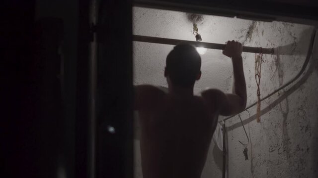 young boy doing pull-ups in a small room. strong teenager doing sports in small room Young short-haired brunette man doing sports in his storage room. with a bar
