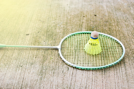 Badminton racket and shuttlecock are on the cement floor, fair lighting.