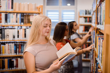 Student girls in the university library, looking for materials for their research. Blond female is...