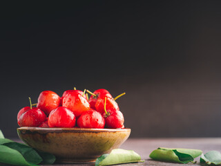 Ripe red cherries in a ceramic bowl with sunlight on black wall background. Space for text. Sweet organic berries. Concept of healthy fruits