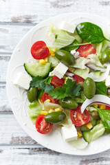Healthy Salad with Feta Cheese, Green Olives, Baby Spinach, Cucumber, Cherry Tomatoes and Capers. Bright wooden background. Top view. Close up.	
