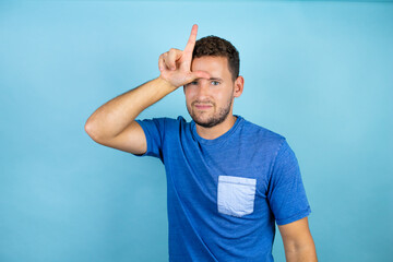 Young handsome man wearing blue casual t-shirt over isolated blue background making fun of people...