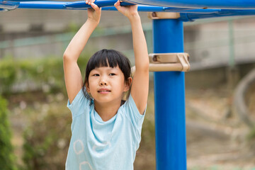 Obraz premium 真夏の公園で雲梯遊具を遊んでいる可愛い子供