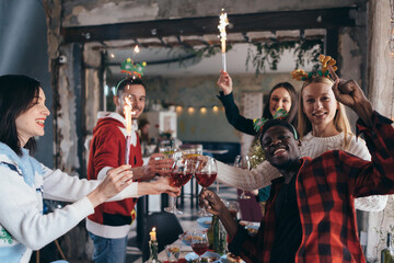 Multi-ethnic friends toasting wine. Young men and women having a party in cafe. Christmas.