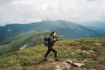 Fototapeta na wymiar Active lifestyle. Young woman tourist in hiking wear and with a backpack climbs to the top of the mountain using hiking poles