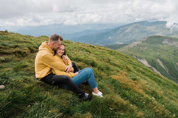 Fototapeta na wymiar A man and a woman in love sit on the top of a mountain and sensual hugging with a scenic nature views around them