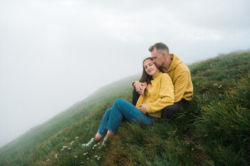Naklejka na ściany i meble Love in the mountains. A loving couple of Caucasian ethnicity hugging while sitting on the top of the mountain, enjoying each other, the landscape and harmony
